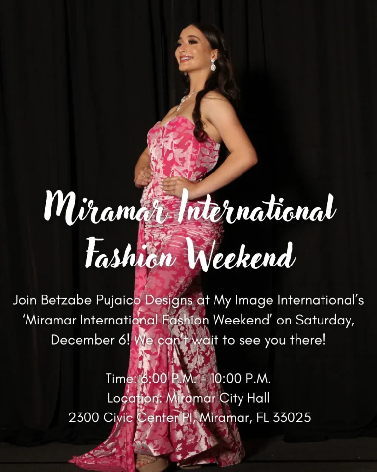 Image of woman standing in front of black backdrop. She is wearing a pink dress adorned with a leaf pattern that fades into grey. Image was taken at Miramar International Fashion Weekend.
